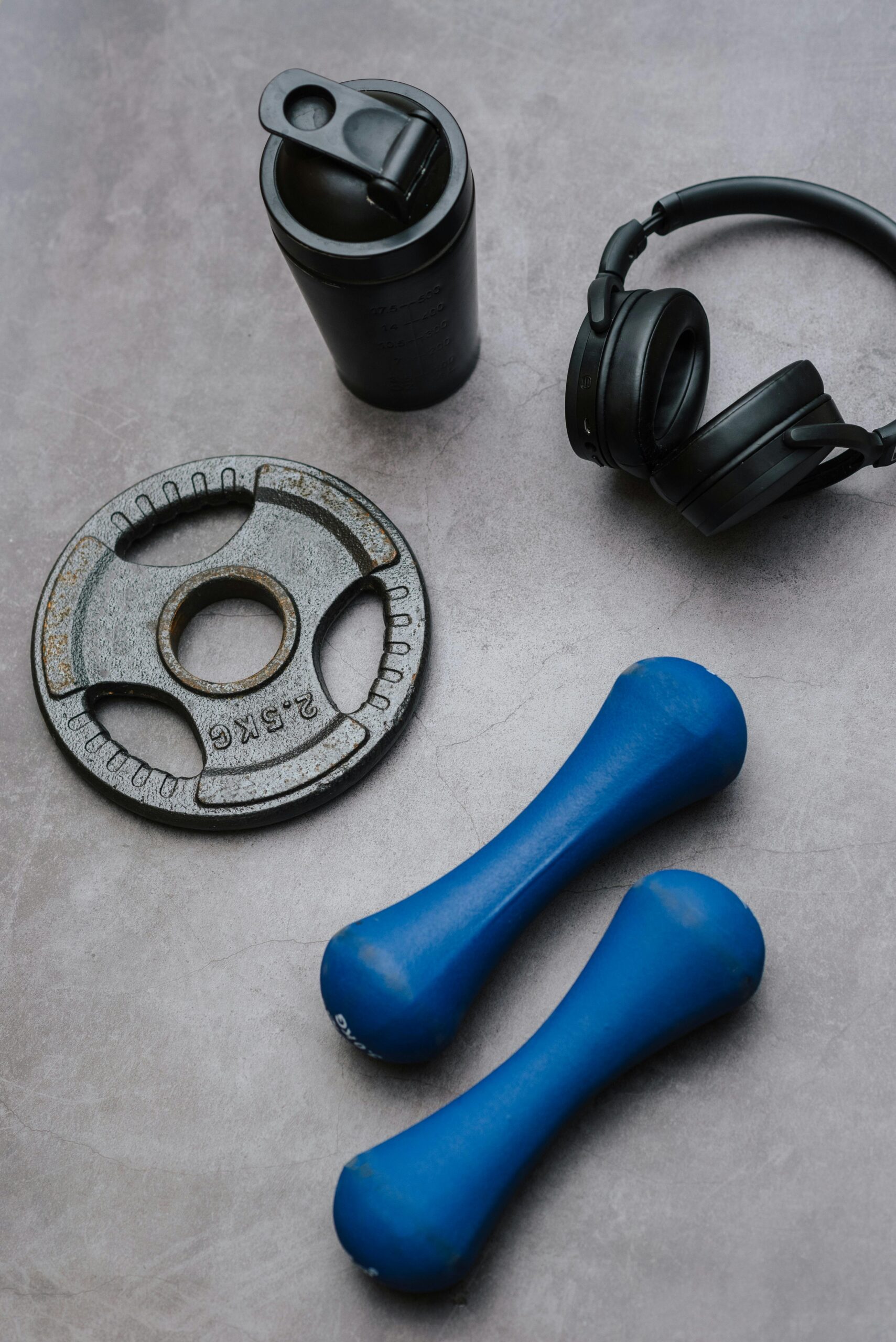 Gym essentials flat lay with dumbbells, weight plate, protein shaker, and wireless headphones